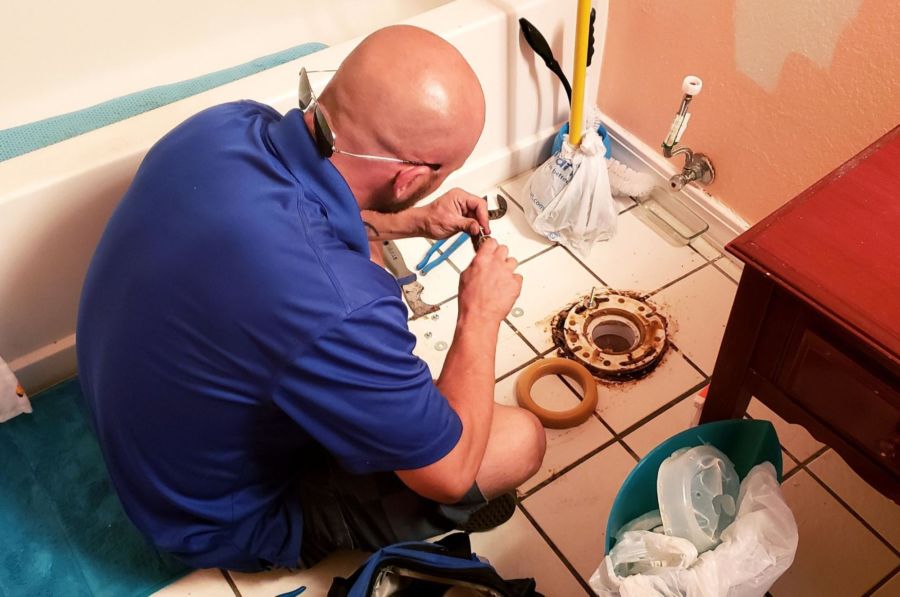 A man sitting on a bathroom floor fixing a toilet ring